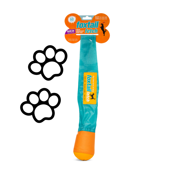 A teal and orange Foxtail Fetch (Dog Toy) with a fabric tail is shown on a white background. Two black paw print graphics appear to the left of this slobber-free, durable toy.