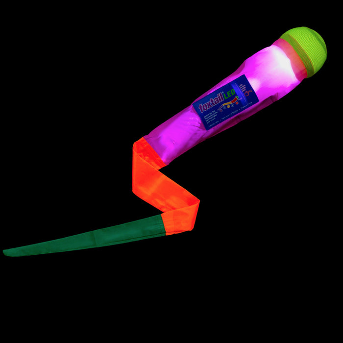 The Foxtail LED is a colorful light-up night toy with a green-rounded end, glowing pink body, and red-green ribbon, ideal for outdoor games and shown against a black background.